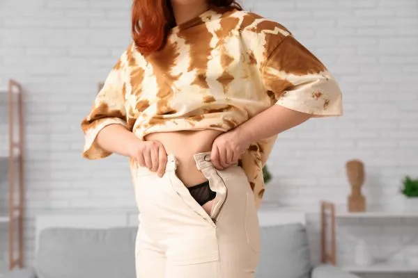 Image of woman trying to do her trousers up after pregnancy weight gain Irthlingborough