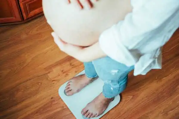 Image of woman weighing herself and experiencing weight gain through pregnancy Irthlingborough